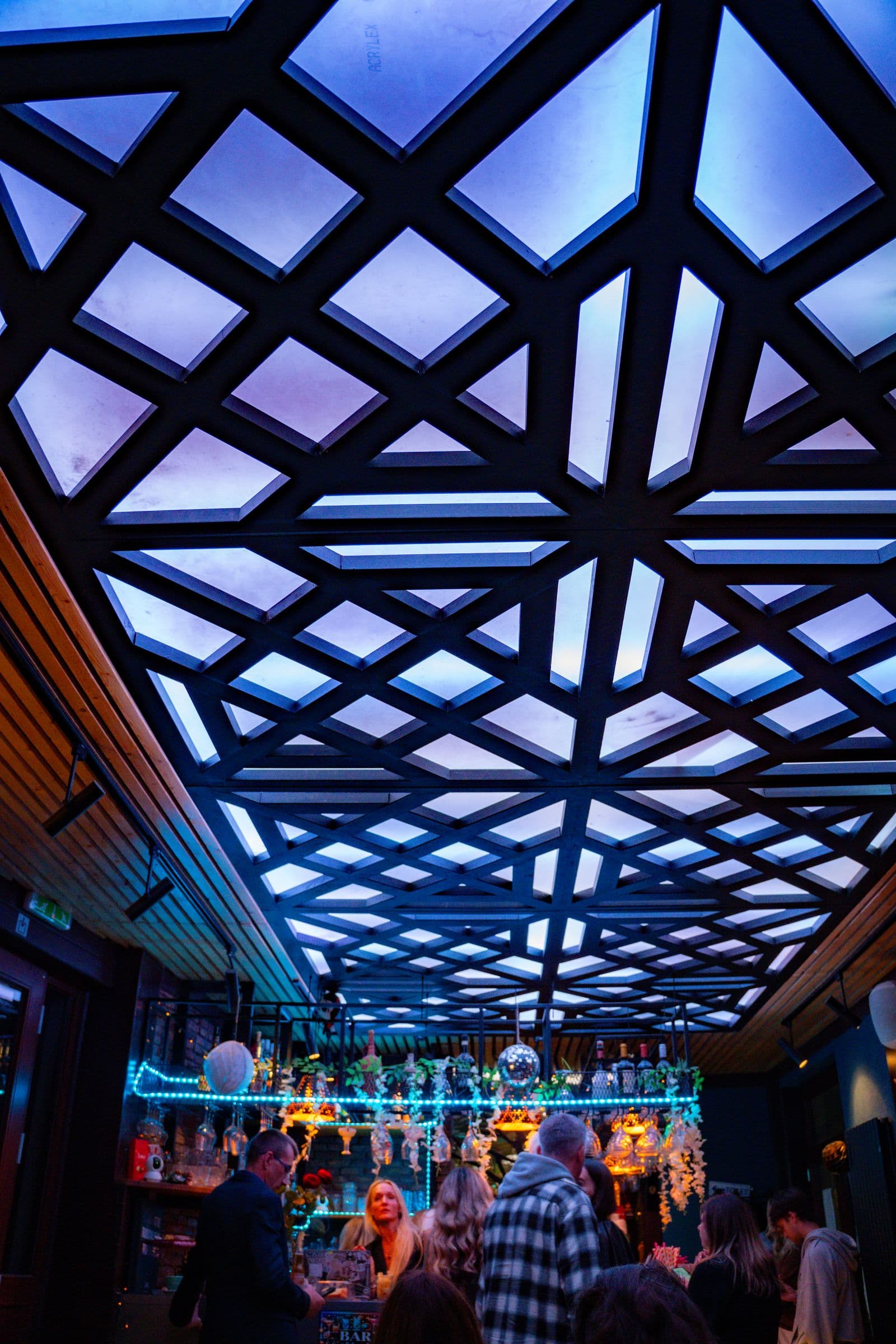 The geometric ceiling lit blue over a full bar.