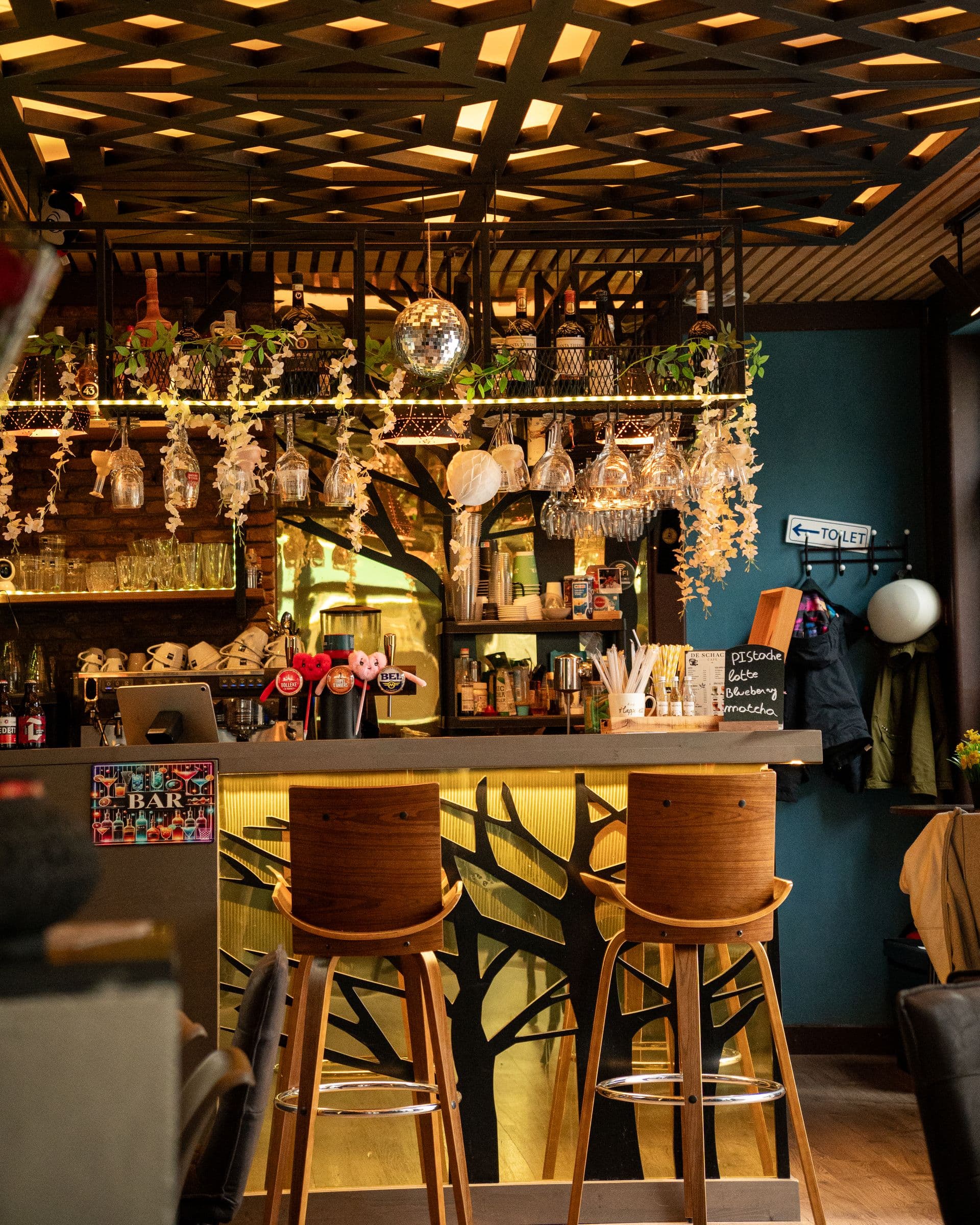 The bar by day: stools, hanging glasses, the lattice ceiling and the tree cut into the counter.