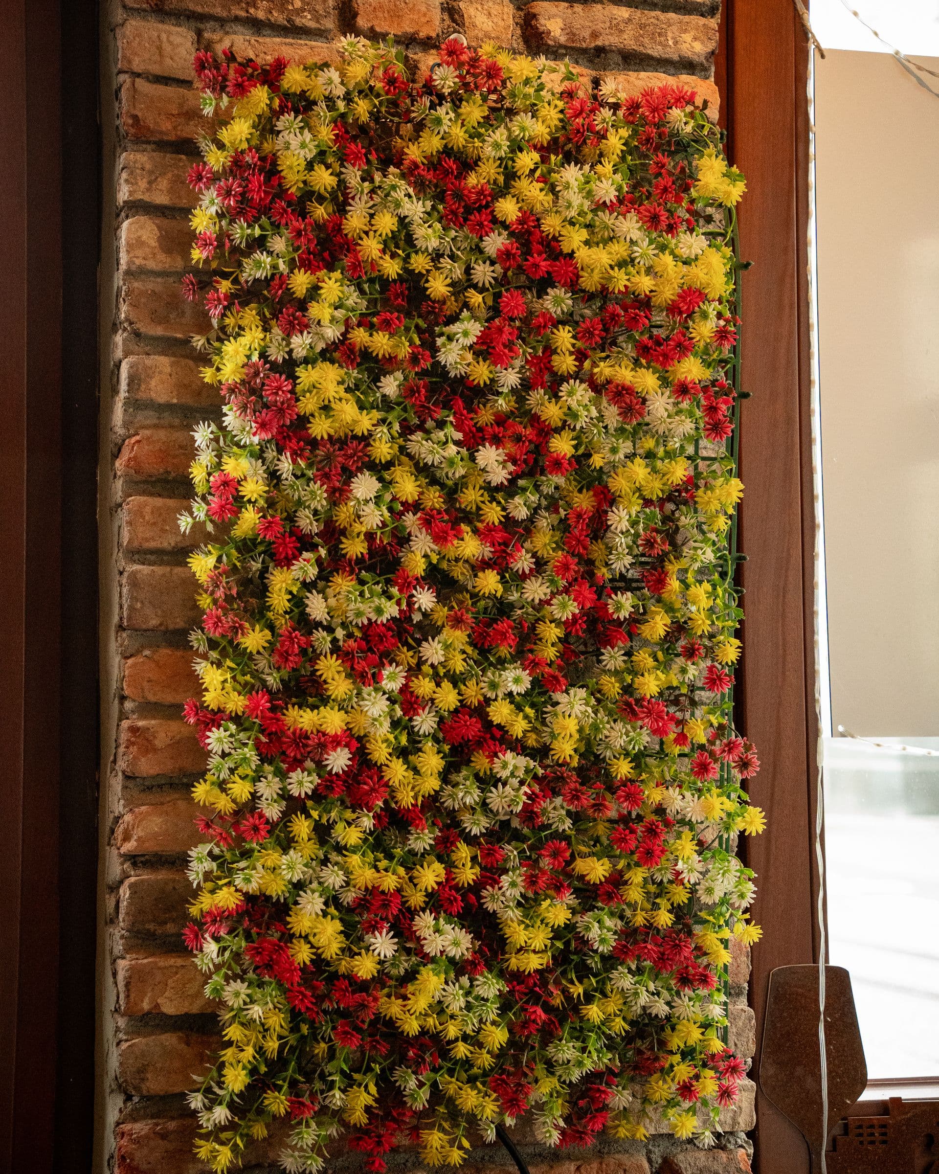 A wall of red, yellow and white flowers against old brick.