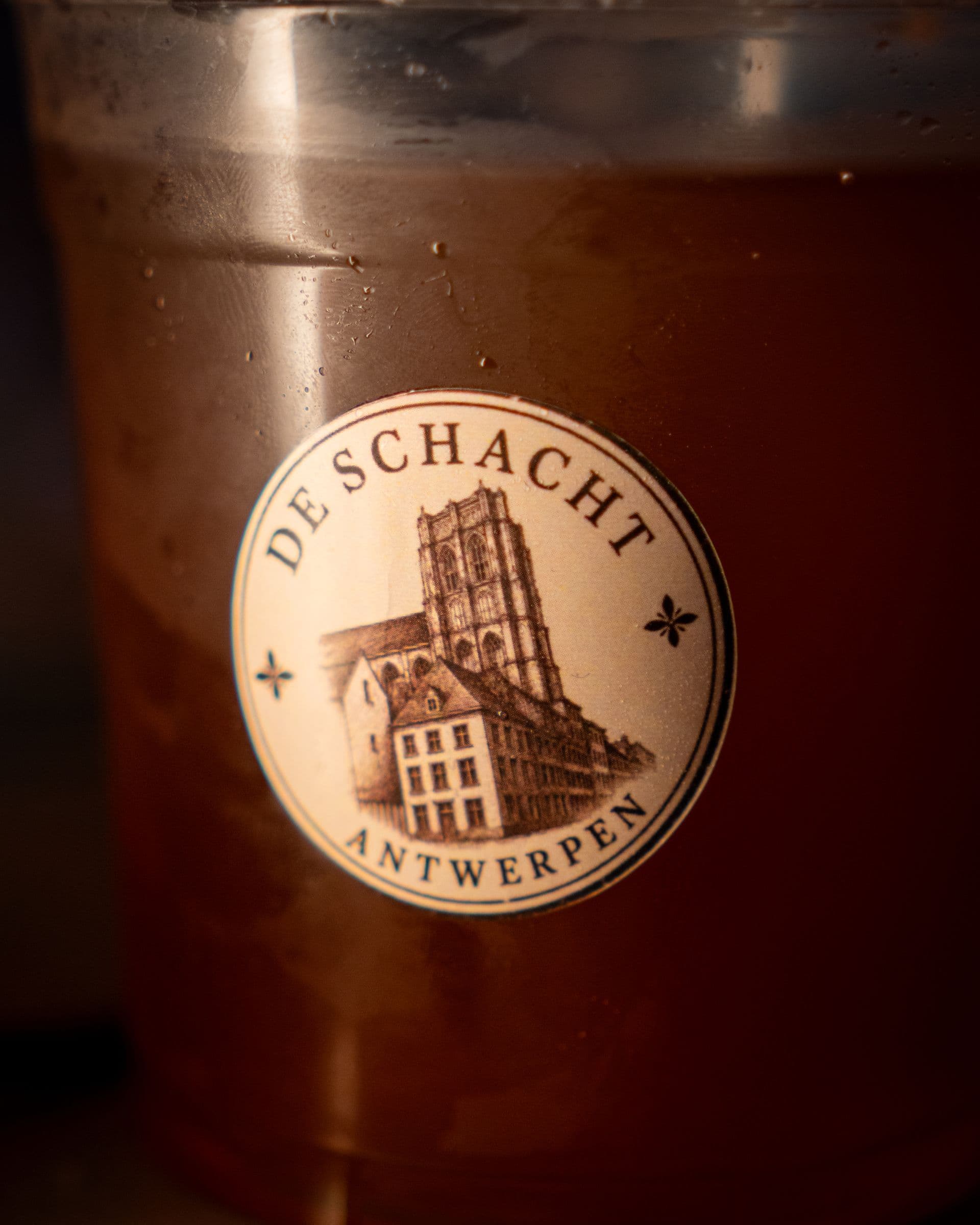 An iced drink in a cup printed with the De Schacht building badge.